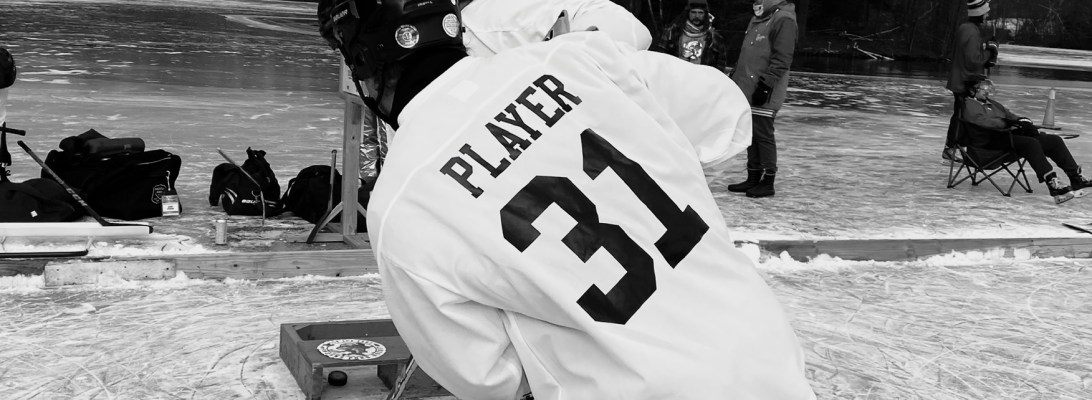 Black and white photo of a hockey player wearing a jersey with the text "Player 31" written on the back. The player is passing the puck.